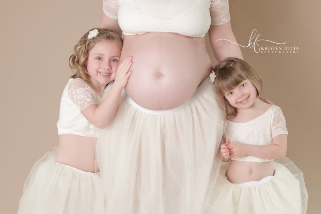 sisters hugging mom's pregnant belly matching cream tutu dresses