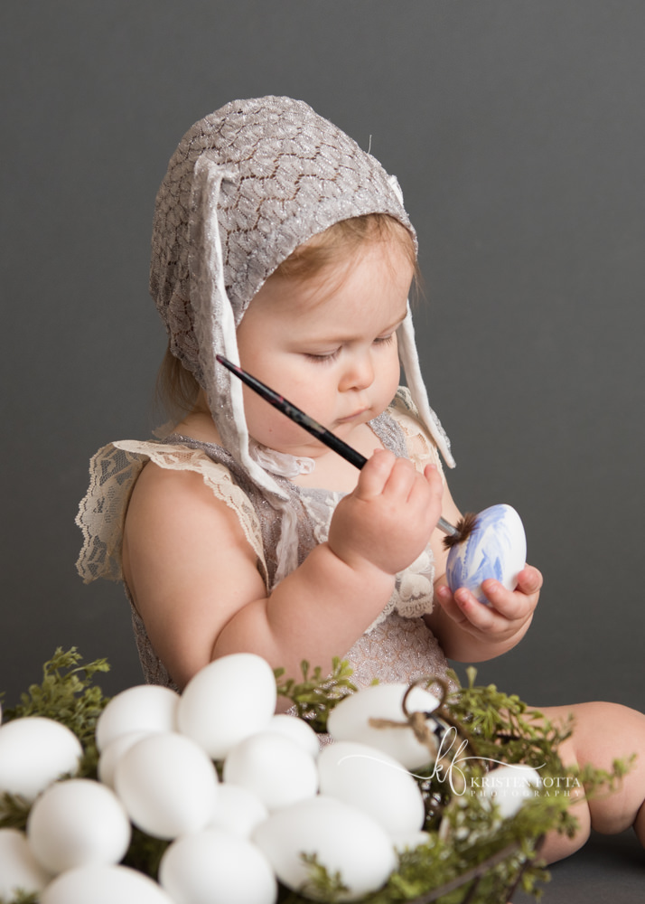 baby girls wearing vintage inspired lace romper and bunny ear bonnet painting an Easter egg